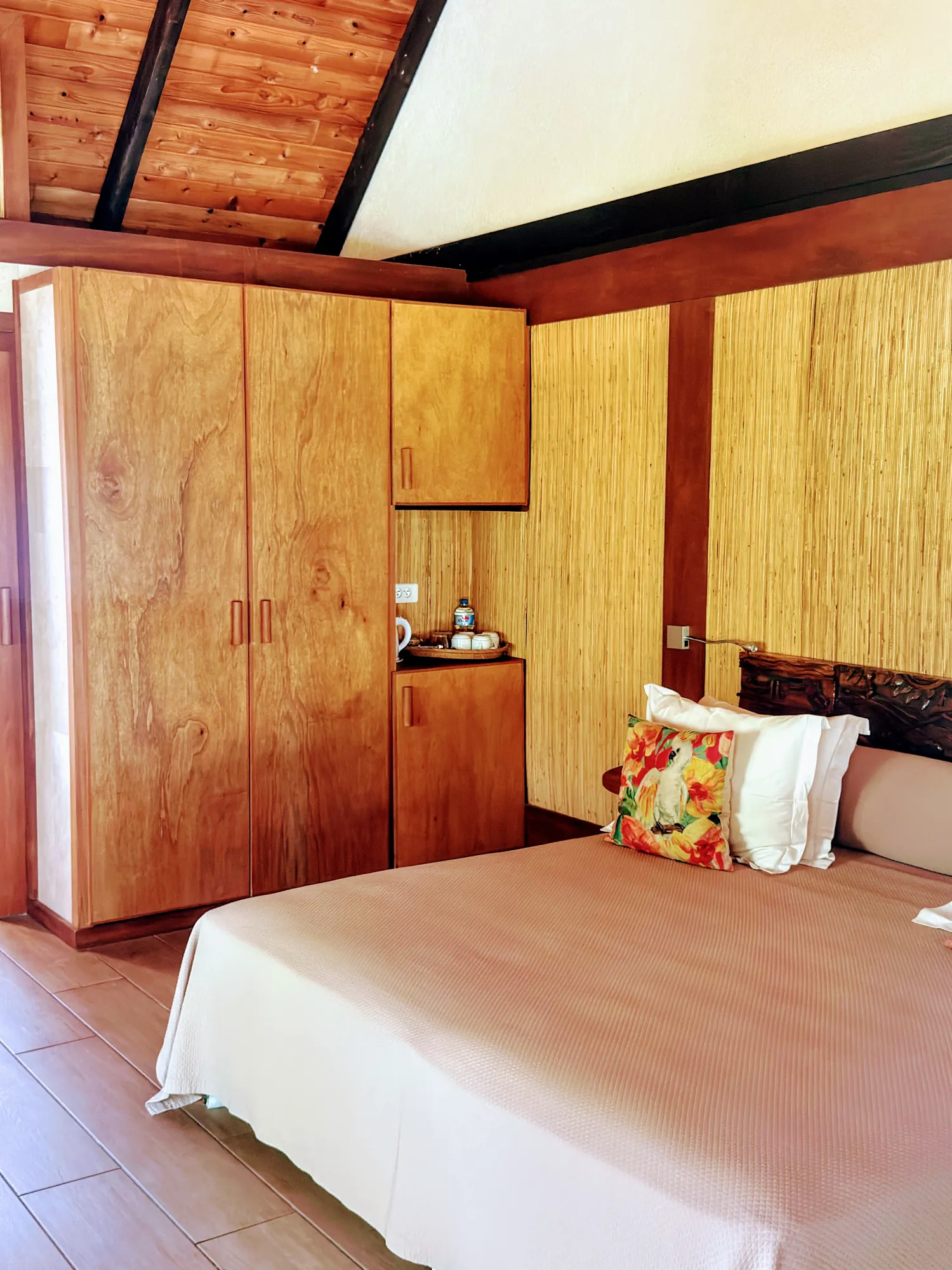 Chambre d'un bungalow traditionnel avec boiseries et coussin fleuri, Hôtel Le Mahana, Huahine