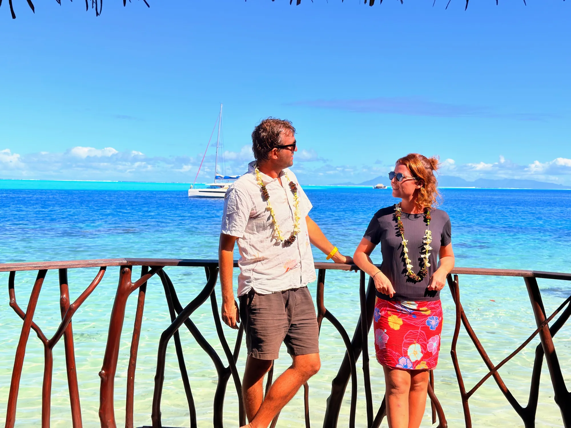 Couple portant des colliers de fleurs sur un ponton face au lagon turquoise, Hôtel Le Mahana, Huahine