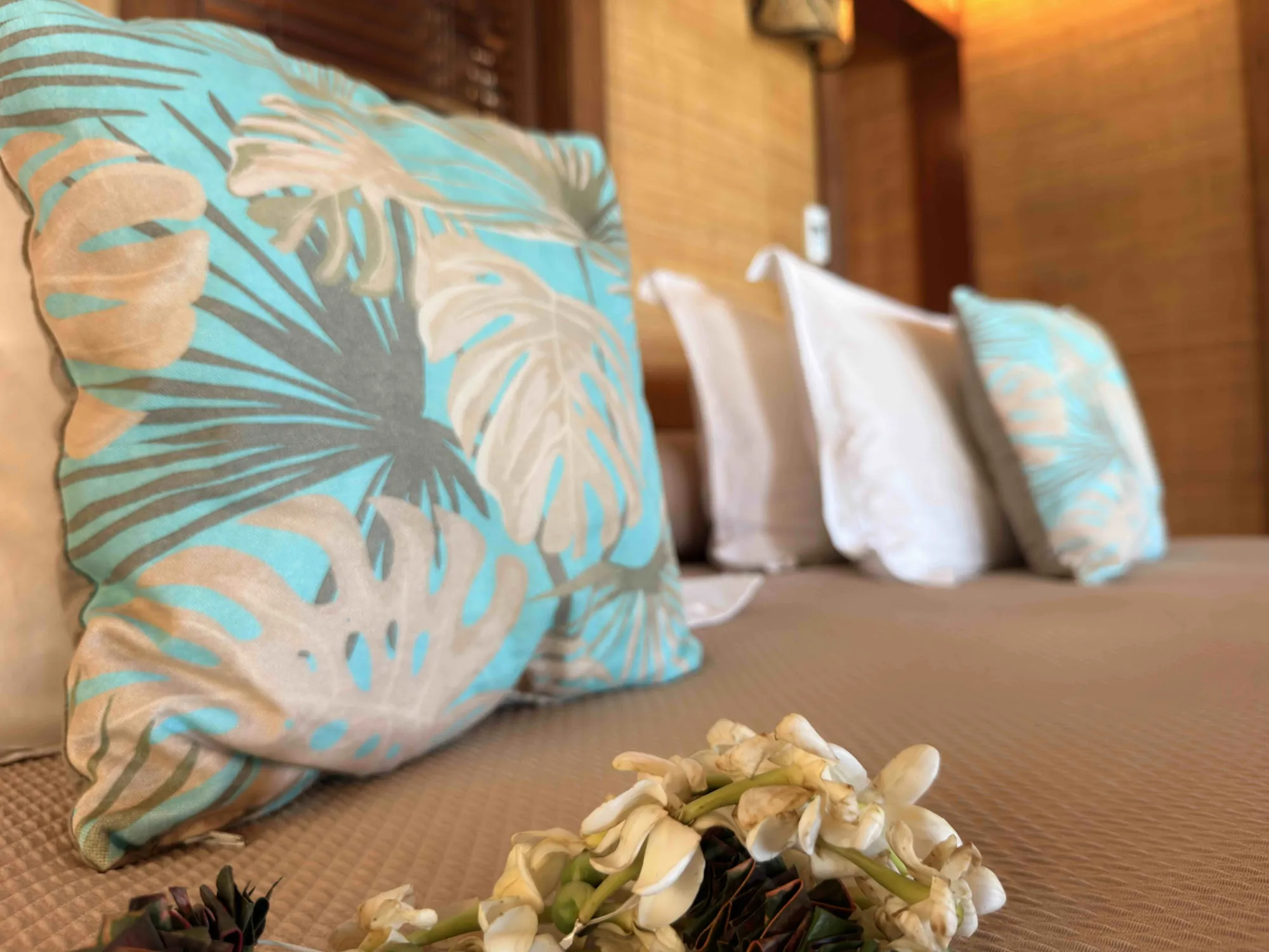 Coussins à motifs tropicaux et couronne de fleurs de tiaré sur le lit, Hôtel Le Mahana, Huahine